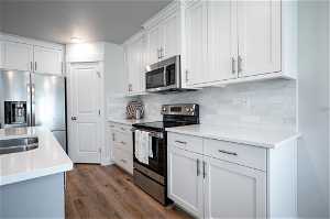 Kitchen featuring white cabinetry, stainless steel appliances, backsplash, and dark wood-type flooring