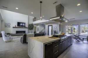 Kitchen with light stone counters, decorative light fixtures, island exhaust hood, a fireplace, and a kitchen island