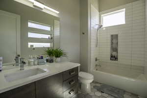 Full bathroom with tiled shower / bath, toilet, vanity with extensive cabinet space, and tile floors