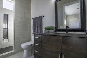 Bathroom featuring vanity, a tile shower, toilet, and tile flooring