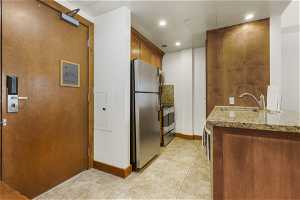 Kitchen with range, stainless steel refrigerator, light stone counters, light tile floors, and sink