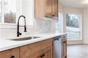 Kitchen featuring stainless steel dishwasher, sink, backsplash, and light hardwood / wood-style floors