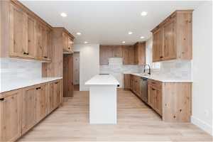 Kitchen featuring light wood-type flooring, a kitchen island, sink, and backsplash