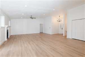 Unfurnished living room featuring ceiling fan with notable chandelier and light hardwood / wood-style floors