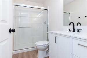 Bathroom with a shower with shower door, hardwood / wood-style floors, vanity, and toilet