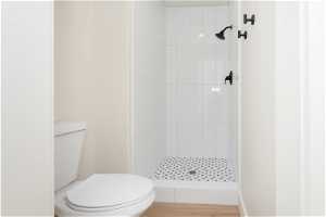 Bathroom with tiled shower, hardwood / wood-style flooring, and toilet