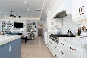Kitchen with tasteful backsplash, custom exhaust hood, light wood-type flooring, ceiling fan, and white cabinetry