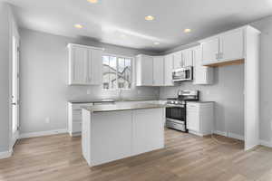 Kitchen with stainless steel appliances, light hardwood / wood-style flooring, and white cabinets