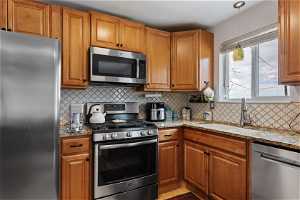 Kitchen featuring appliances with stainless steel finishes, sink, light stone countertops, and backsplash