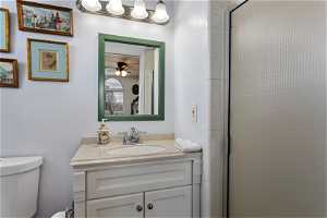 Bathroom with a shower with shower door, vanity, toilet, and ceiling fan