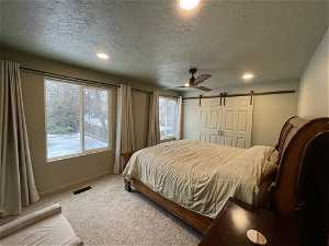 South unit Primary bedroom with a textured ceiling, a barn door, and ceiling fan