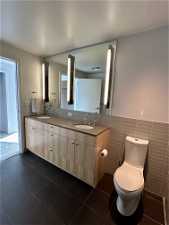 Bathroom featuring tile floors, double sink, vanity with extensive cabinet space, and tile walls