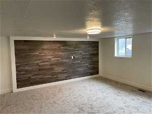 Basement featuring dark colored carpet, wood walls, and a textured ceiling