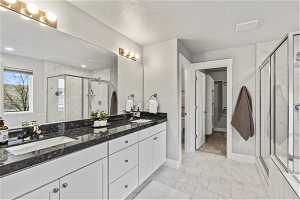 Primary bathroom with a textured ceiling, dual vanity, tile flooring, and walk in shower
