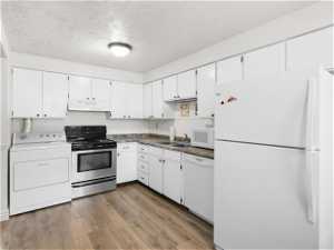 Kitchen with hardwood / wood-style floors, washer / dryer, sink, white appliances, and white cabinetry