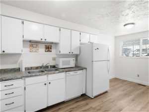 Kitchen with white cabinets, sink, white appliances, and light hardwood / wood-style floors