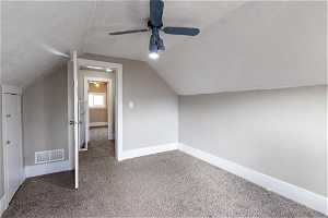 Additional bedroom with a textured ceiling, dark colored carpet, vaulted ceiling, and ceiling fan