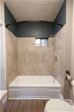 Bathroom with a textured ceiling, hardwood / wood-style floors, toilet, and tiled shower / bath combo