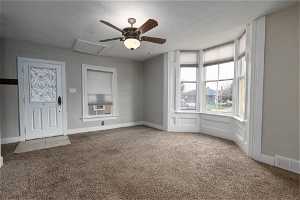 Unfurnished room featuring dark carpet, bay window, a textured ceiling, and ceiling fan