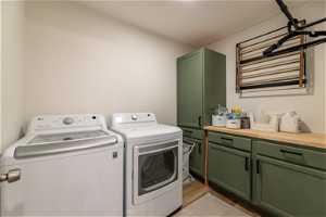 Clothes washing area featuring separate washer and dryer, light wood-type flooring, and cabinets