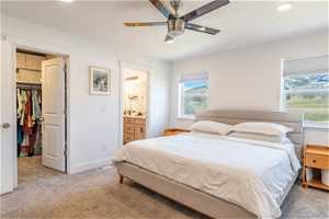 Carpeted bedroom featuring multiple windows, ensuite bathroom, a walk in closet, and ceiling fan