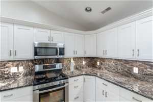 Kitchen featuring appliances with stainless steel finishes, white cabinets, and tasteful backsplash