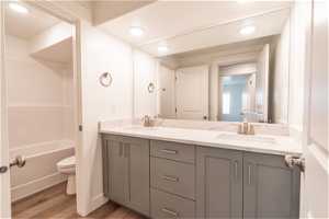 Full bathroom featuring  shower combination, double vanity, toilet, and hardwood / wood-style flooring