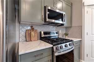 Kitchen featuring stainless steel appliances, gray cabinets, backsplash, and light stone countertops