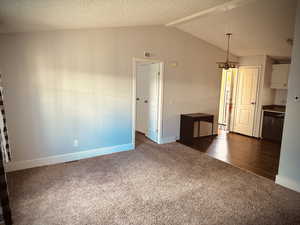 Unfurnished room with dark colored carpet, lofted ceiling, and a textured ceiling