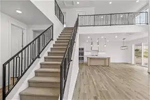 Staircase featuring a towering ceiling, an inviting chandelier, and light hardwood / wood-style floors
