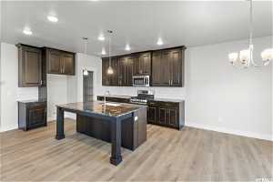 Kitchen with stainless steel appliances, dark stone countertops, a notable chandelier, sink, and light hardwood / wood-style flooring