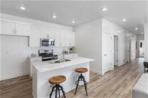 Kitchen featuring an island with sink, white cabinets, light hardwood / wood-style floors, stainless steel appliances, and a kitchen bar