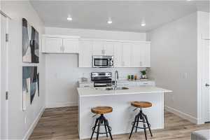 Kitchen featuring white cabinetry, stainless steel appliances, light wood-type flooring, and a kitchen island with sink