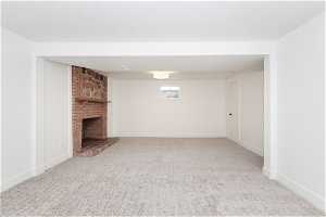 Unfurnished living room featuring a fireplace, a textured ceiling, brick wall, and light colored carpet
