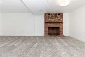 Unfurnished living room featuring a textured ceiling, dark colored carpet, a brick fireplace, and brick wall