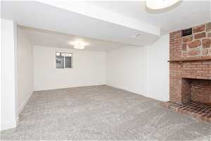 Basement featuring a brick fireplace, a textured ceiling, brick wall, and dark colored carpet