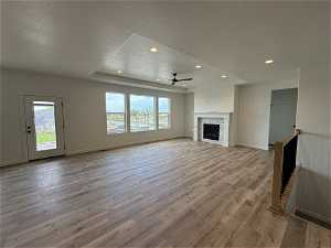 Unfurnished living room with ceiling fan, hardwood / wood-style flooring, a fireplace, and a tray ceiling