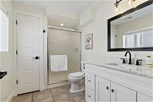 Bathroom with tile floors, a shower with shower door, oversized vanity, and toilet