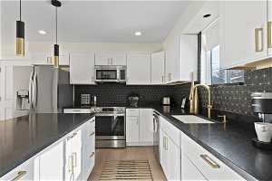 Kitchen featuring pendant lighting, tasteful backsplash, appliances with stainless steel finishes, white cabinets, and sink