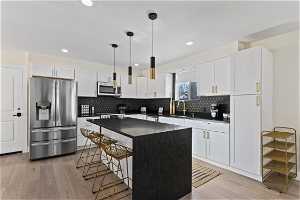 Kitchen with a center island, white cabinetry, light hardwood / wood-style floors, and stainless steel appliances