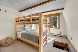Bedroom featuring a baseboard heating unit, beam ceiling, and light colored carpet.