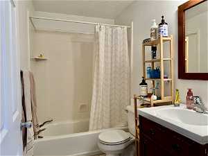 Full bathroom with shower / tub combo, a textured ceiling, large vanity, and toilet