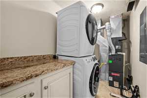 Clothes washing area with stacked washer / drying machine, cabinets, and a textured ceiling