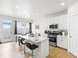 Kitchen featuring stainless steel appliances, a notable chandelier, decorative light fixtures, white cabinets, and light wood-type flooring