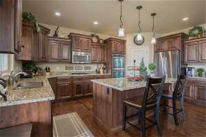 Kitchen with stainless steel appliances, decorative light fixtures, a breakfast bar area, light stone countertops, and dark hardwood / wood-style flooring