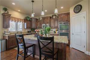 Kitchen featuring appliances with stainless steel finishes, light stone counters, and dark hardwood / wood-style floors