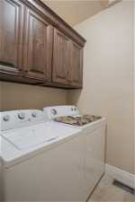Clothes washing area with cabinets, washing machine and clothes dryer, and light tile floors