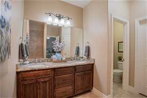 Bathroom with large vanity, toilet, double sink, and tile floors