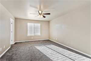 Empty room featuring dark colored carpet and ceiling fan