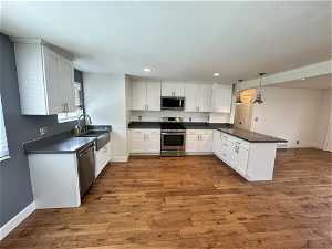 Kitchen with hanging light fixtures, stainless steel appliances, hardwood / wood-style flooring, and kitchen peninsula